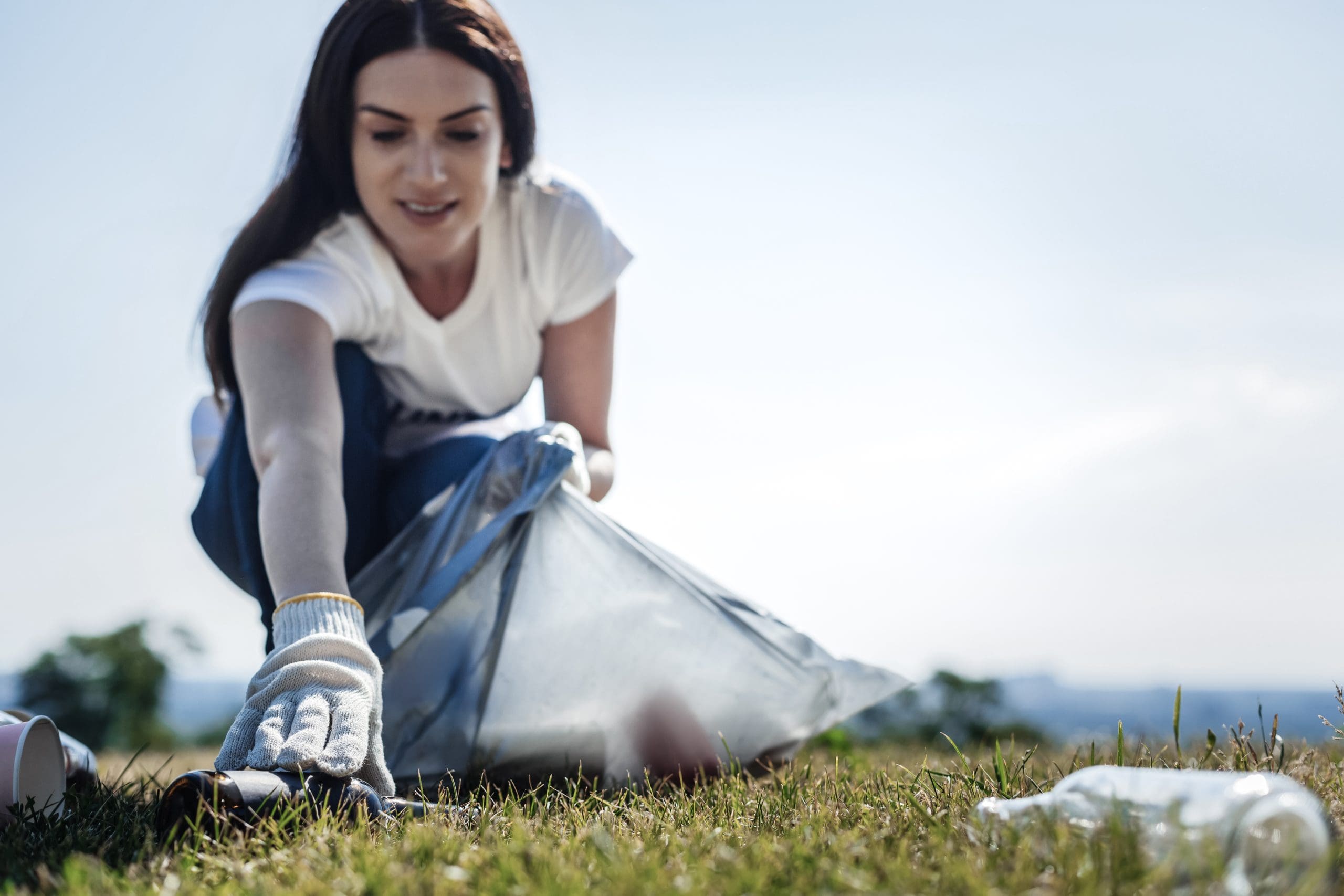 Woman picks up litter from grass, fostering environmental care and community responsibility.