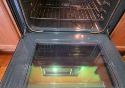 A sparkling clean kitchen oven with an open door, crystal clear glass window, and shiny metal baking racks inside.
