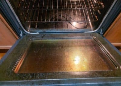 Appliance oven before cleaning service, showing grease smudges on the open glass door and a dirty metal wire rack.
