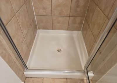 Bathroom shower tray after professional cleaning, showing a sparkling white floor, bright grout lines, and clean tan tiles.