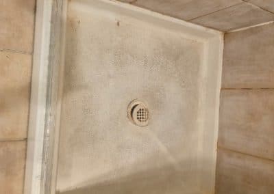 Bathroom shower tray before cleaning, showing a center drain, tan wall tiles, and glass door frame