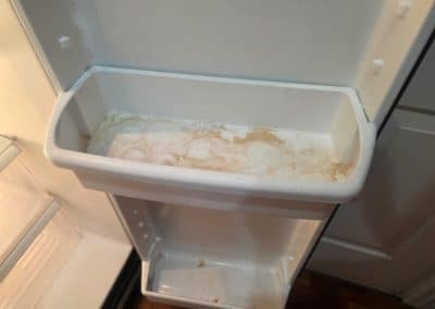 A dirty white plastic refrigerator door shelf covered in brown sticky residue, food stains, and ring marks from bottles.